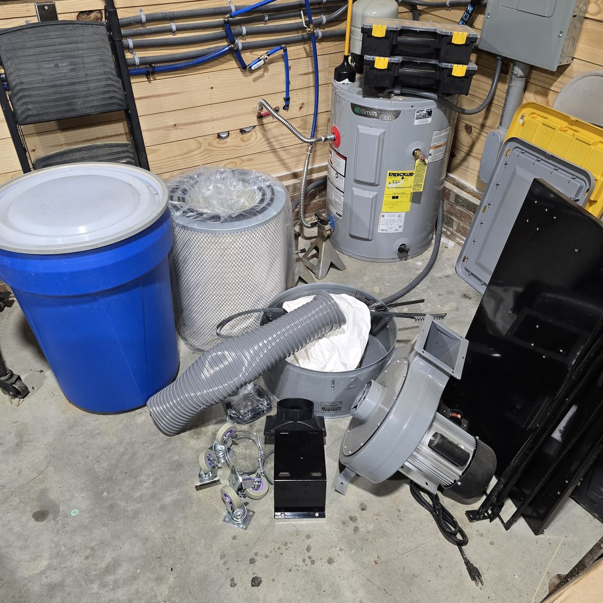 A garage floor crowded with a bin, a filter, ducting, a blower, and parts