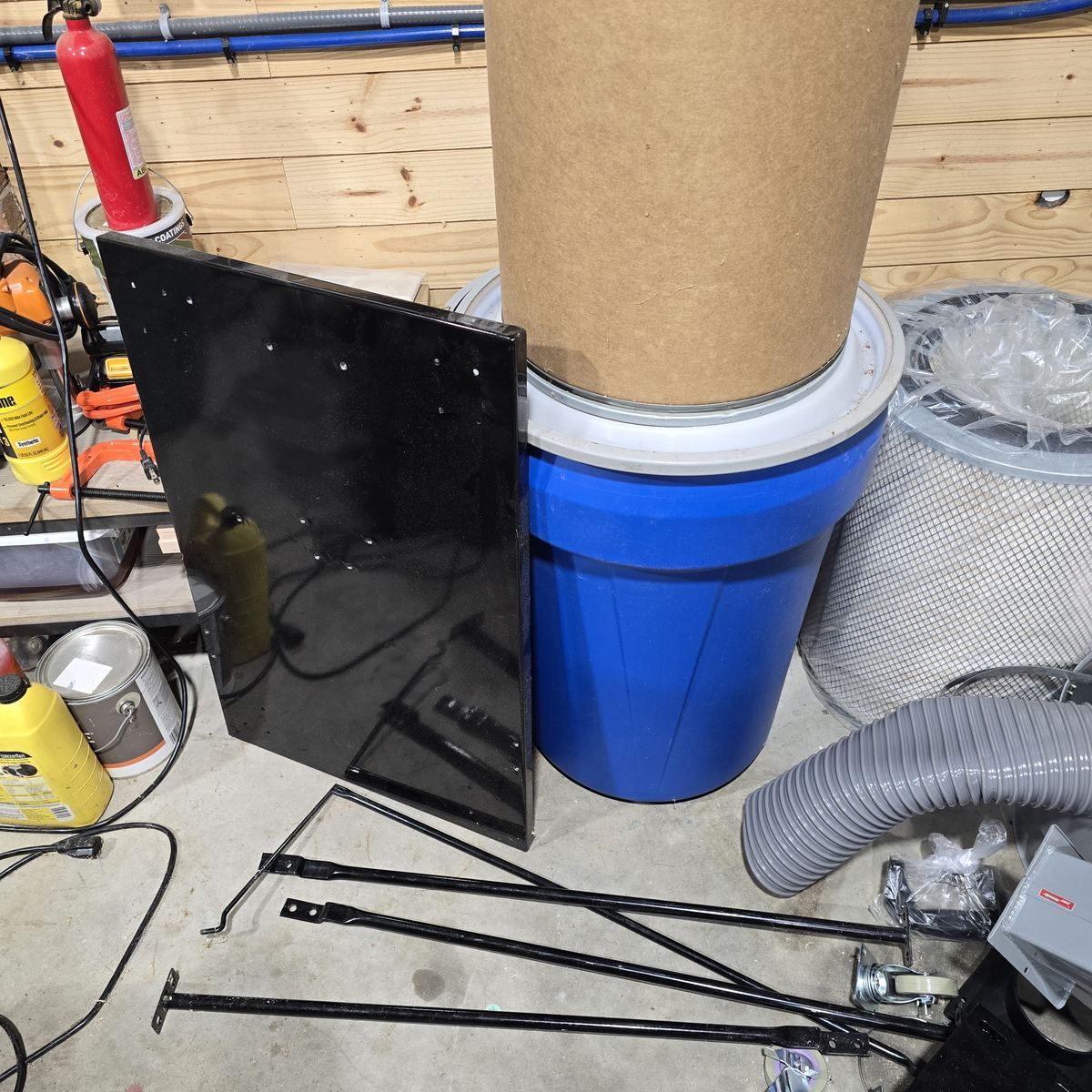 A workshop corner with a bin, a panel, and parts on the floor